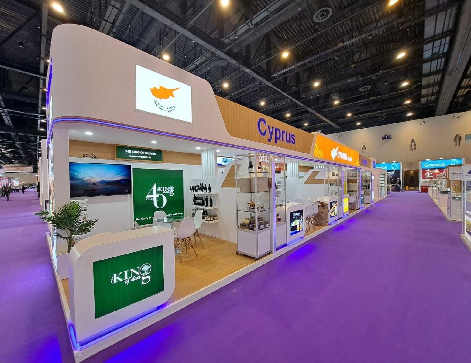 Cyprus national pavilion with a backlit flag panel, orange fascia and glass exporter showcases on a purple aisle