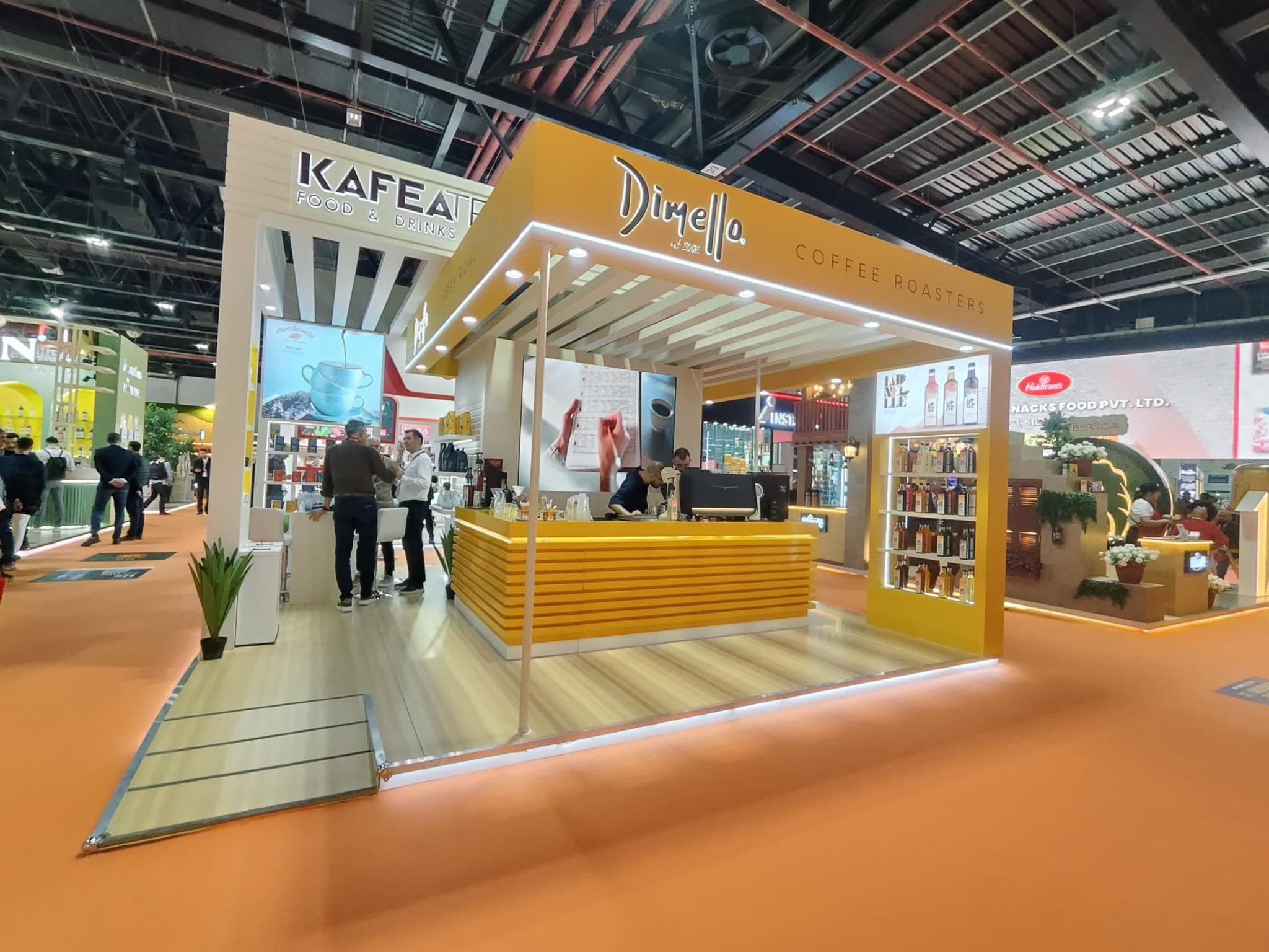 Dimello Coffee Roasters stand, a yellow slatted canopy over a working barista counter and bottle display