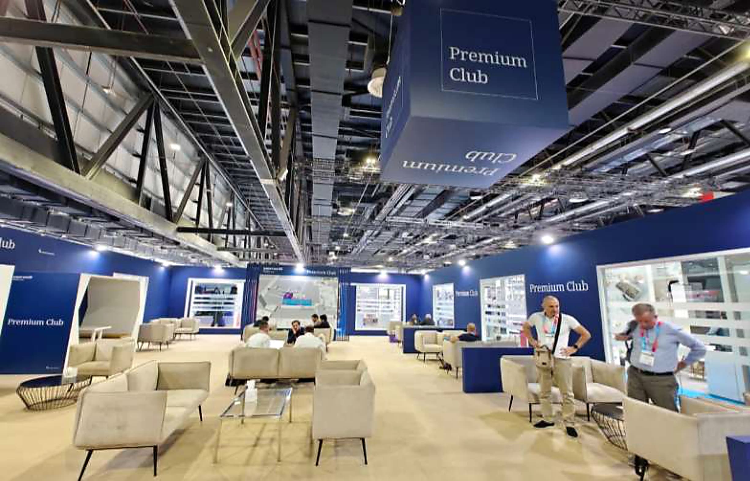 Premium Club exhibitor lounge with a suspended branded cube and upholstered seating groups